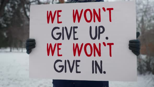 A Person is Standing in the Park Holding a Sign We Wont Give Up We Wont Give In.