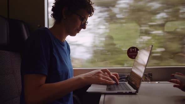 Woman in Glasses Working on a Laptop While Going By Train