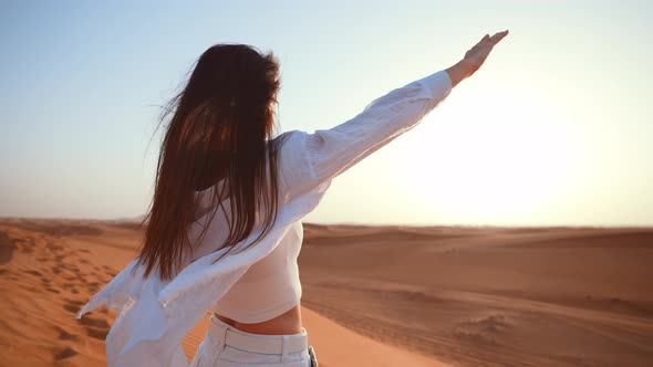 Back View Young Beautiful Caucasian Woman Standing in Sandy Desert and Raises Her Hands Up