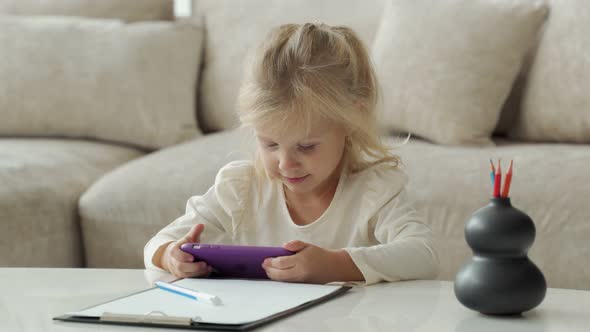 Cute Little Girl with a Smartphone on the Couch in the Room Playing Games