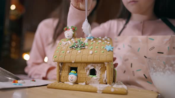 Ginger House with Unrecognizable Little Girl Placing Sugar Icing and Woman Talking at Background