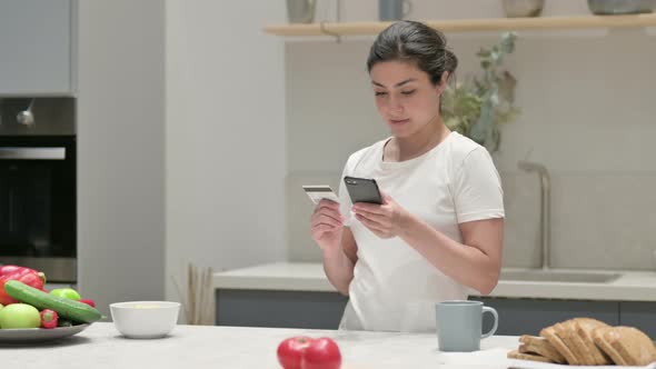 Indian Woman Making Online Payment on Smartphone in Kitchen