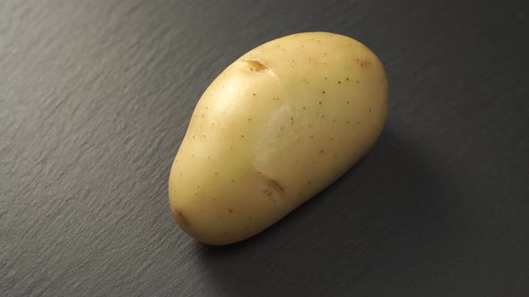 Single uncooked potato on a gray stone background.