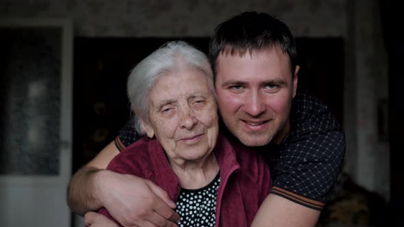 Grandson Son With A Smile Embraces Hugs His Old Elderly Grandmother Mother