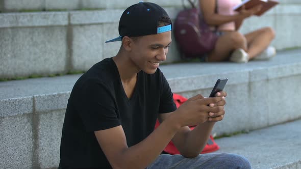 Happy African-American Teenager Chatting Smartphone on Campus Stairs, New App