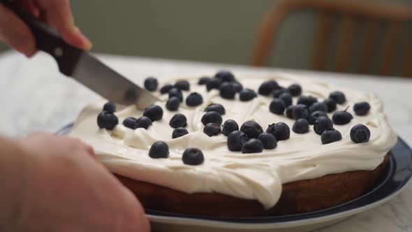 Crop confectioner cutting yummy creamy cake with blueberries