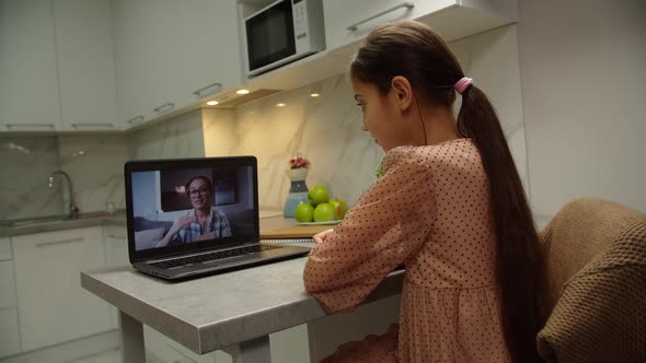 School Girl Listening to Teacher Via Online App on Laptop at Home
