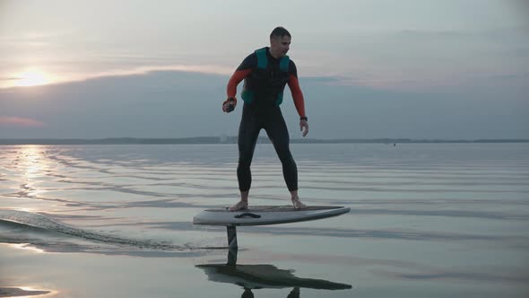 Man Riding on a Hydrofoil Surfboard on Large Blue Lake at the Pink Sunset