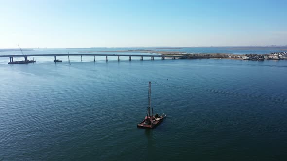 An aerial shot over a dredge on a barge sailing on Grassy Bay in Queens, NY. The camera orbits the d