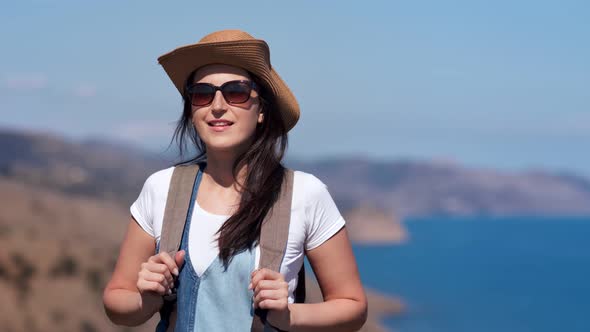 Smiling Beautiful Travel Backpack Woman in Sunglasses and Hat Posing at Summer Seascape Background