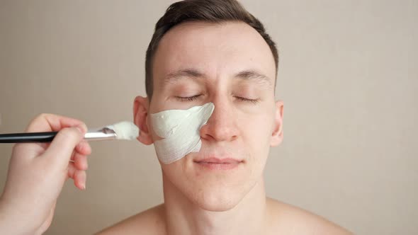 Beautician Applies a Mask to a Man with a Brush on Face