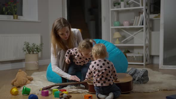 Wide Shot of Musician Mother and Twin Daughters Playing with Guitar in Living Room at Home