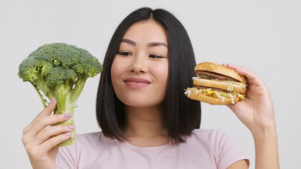 Chinese Lady Holding Broccoli And Burger Choosing Nutrition White Background