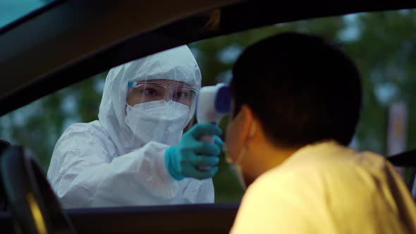 doctor in PPE suit using infrared thermometer measuring temperature of man at drive thru station