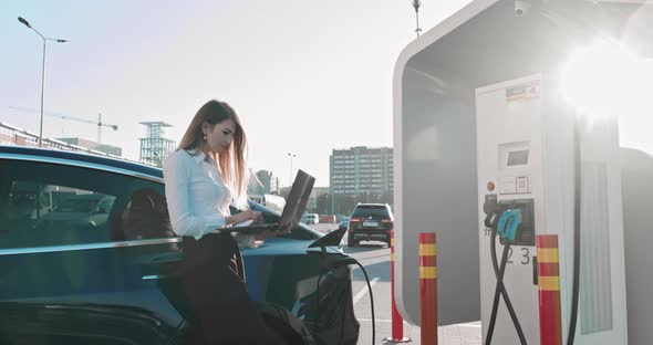 Business Woman Holding Laptop Near Electric Car Car Charging Station
