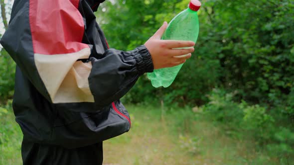 Unrecognizable person throw plastic bottle in nature. Forest pollution