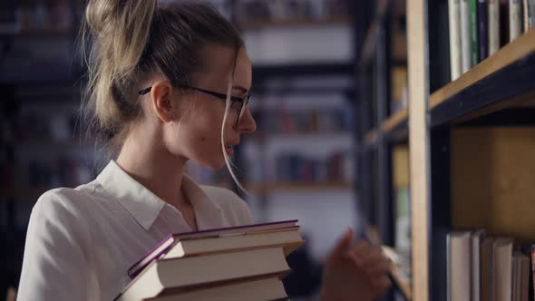 Attractive Woman Holding Pile of Books in the Library Looking for Another