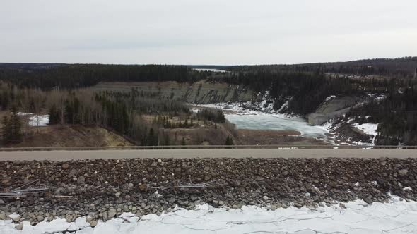 Aerial fly over edge of frozen dam with logging truck passing by