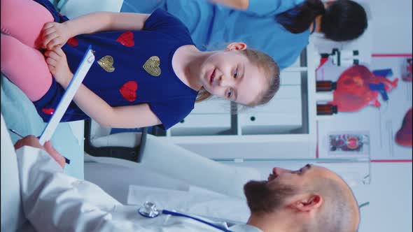 Vertical Video: Doctor Talking with Little Girl Sitting on Bed