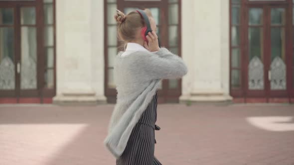 Charming Schoolgirl in Headphones Turning and Walking To School Building. Portrait of Happy Cheerful