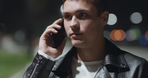 Close Up Portrait of Young Man Talking on Mobile Phone, Walking in Night Park