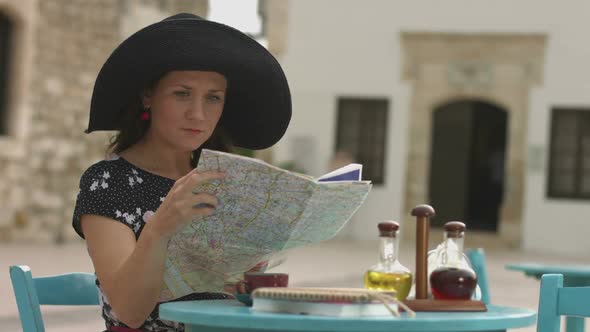 Pretty Female Tourist Sitting in Cafe With Map in Hands, Examining Journey Route