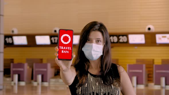 Woman, in Protective Mask, Holds Smartphone with COVID-19 Icon, Text - Travel Ban