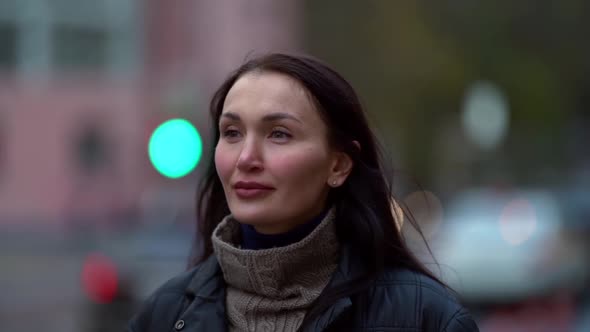 Portrait of a Middle-aged Dark-haired Woman in a Black Jacket Walking on a City Street on an Autumn