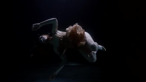 Underwater Shot with Floating Young Woman in Silk Dress Slow Motion in Water Deep and Darkness