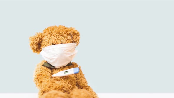 Panning Video of Toy Bear Sits in Mask on Light Background with Thermometer