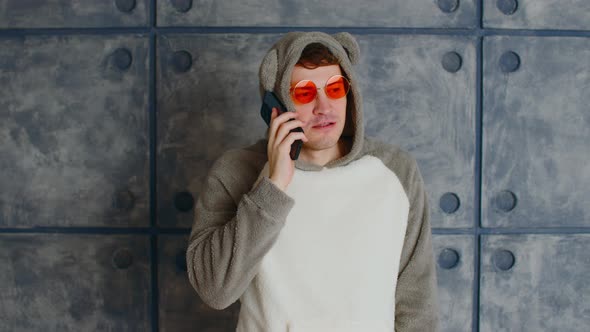 Young Man in Bright Glasses with Smartphone Near Patterned Concrete Wall