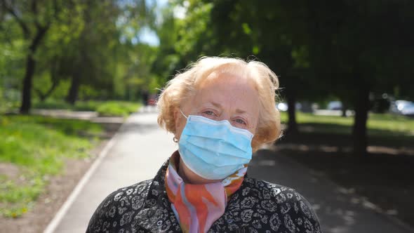 Portrait of Old Woman with Medical Face Mask Stands at City Street. Grandmother Wears Protective