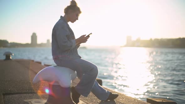 Slowmotion Side View of Dreamy Romantic Girl with Blond Hair in Denim Sitting in Concrete Pier Near