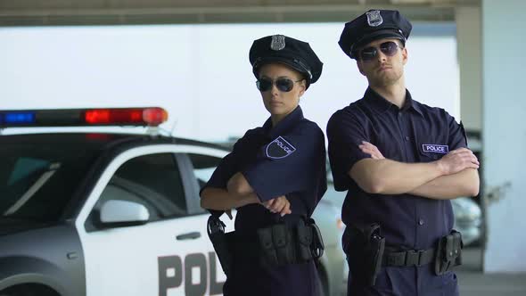 Confident Police Teammates in Uniform and Sunglasses Standing Against Patrol Car