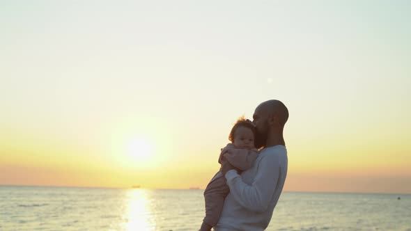 Caucasian Man Holding His Daughter in His Arms Lifts Her Top and Kisses