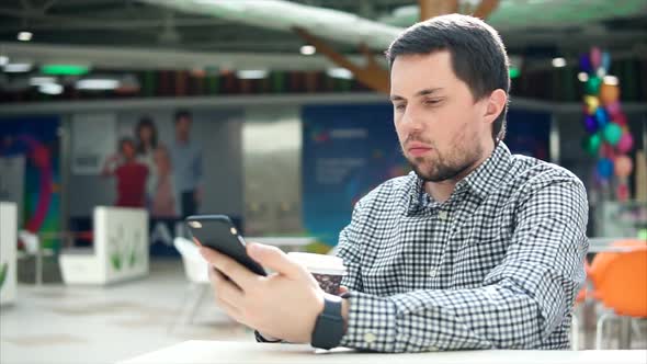 Man Using Smart Phone and Drinking Coffee in Shopping Centre