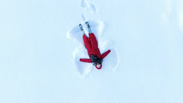 Girl in a Red Down Coat Making a Snow Angel. Aerial, Camera Rises Up in a Spiral, Top View