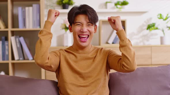 Young man gesturing Yes, smiling at camera to celebrating successful. Posing on couch in the living