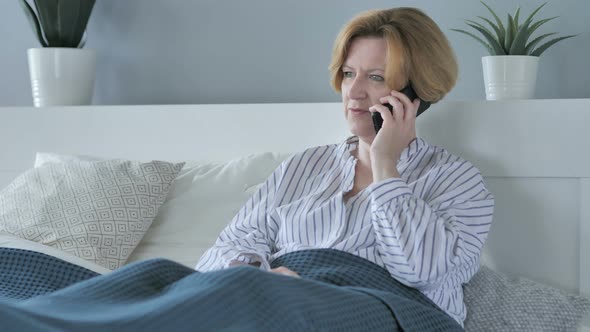 Old Senior Woman Talking on Phone while lying in Bed