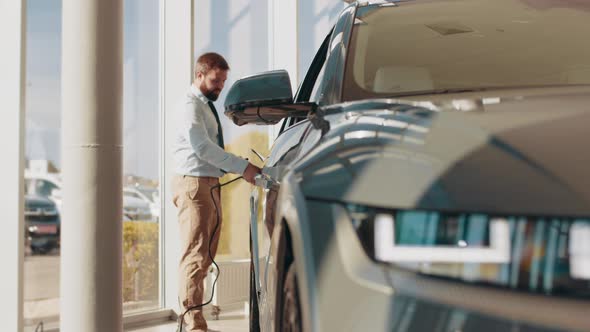 Handsome Business Man Holding Charging Cable for Electric Car