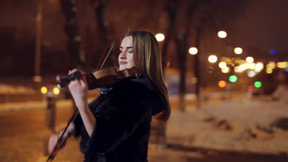 Young girl playing violin outdoors. Professional violinist woman with the violin at late evening