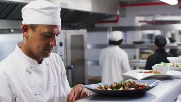 Caucasian male chef garnishing dish and smiling in restaurant kitchen