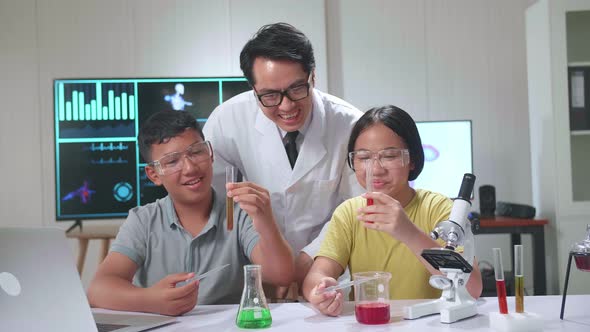 Excited Asian Boy And Girl Learning Science Experiment In Laboratory With Teacher In Classroom