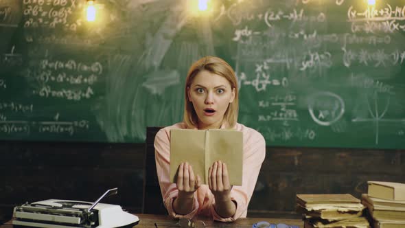 Student Studying on Chalkboard. Portrait of Young Surprised Woman Holding Book Against Blackboard