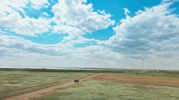 Car Moving By Rustic Road on Wind Electric Generators Background