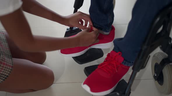 High Angle View Feet of Disabled Man on Legrest with Unrecognizable Teenage Girl Tying Shoelaces on