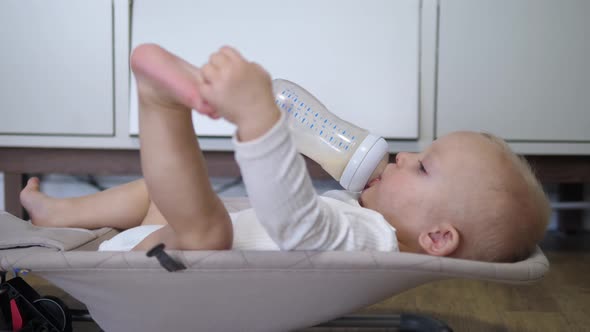 Hungry White Baby Has Almost Finished His Milk Bottle Playing with Feet