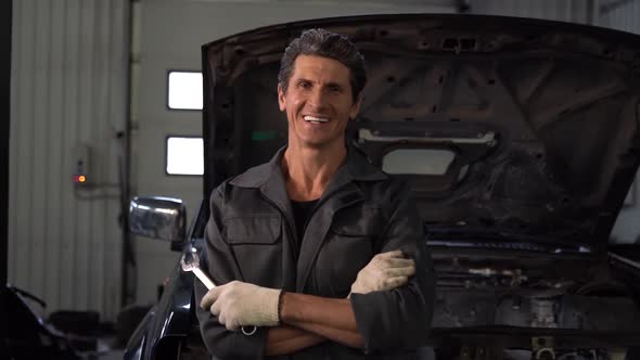 Portrait view of the smiling senior auto mechanic wearing gloves standing near the car