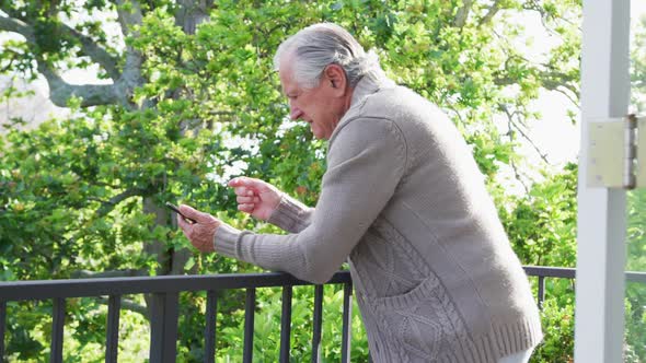 Side view of senior man leaning on railing while using smart phone in balcony
