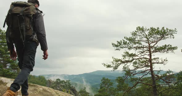 The Man is Coming Out on Top of the Cliff and Looking at the Landscape